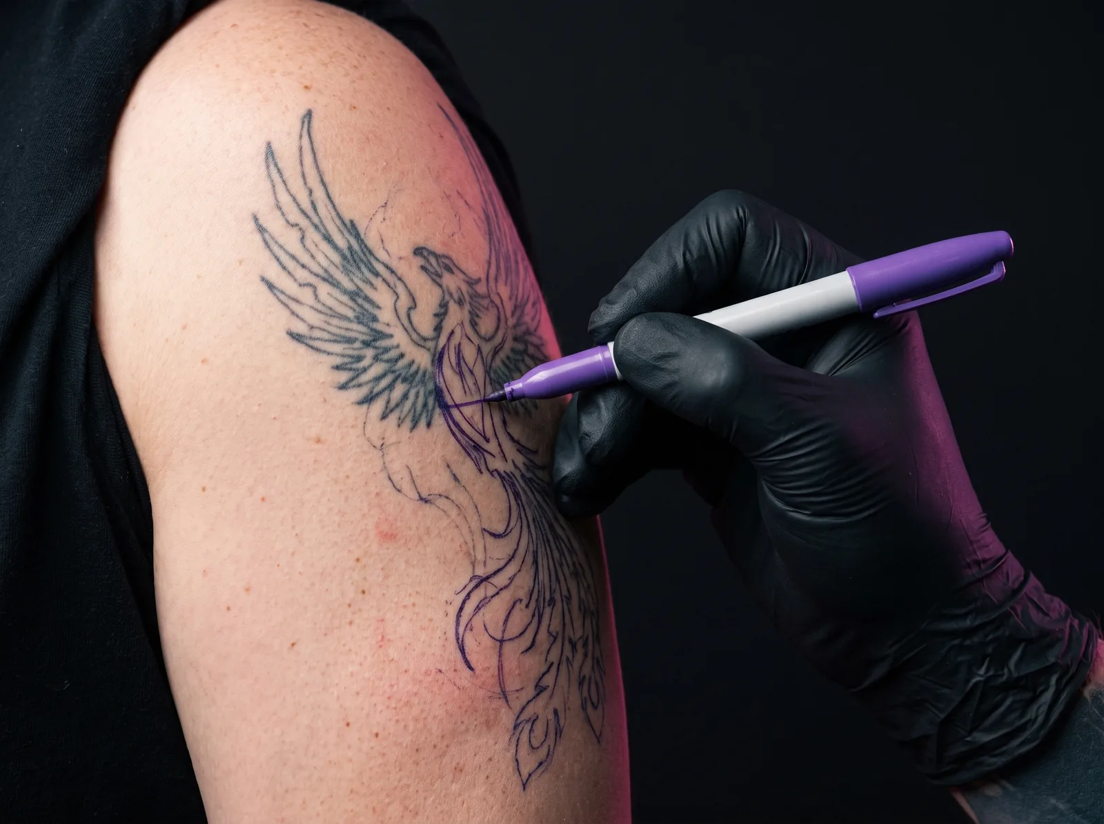 Artist sketching a cover-up design directly over an existing tattoo during a consultation
