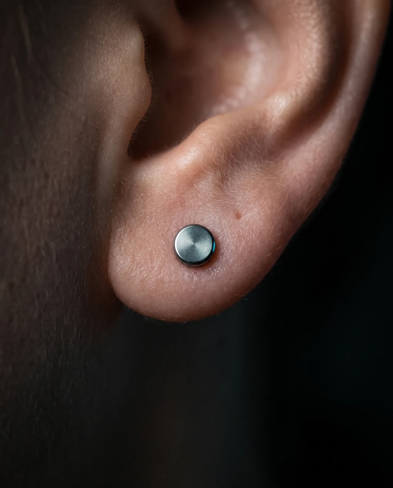 Close-up of a healed ear lobe piercing with a simple titanium stud