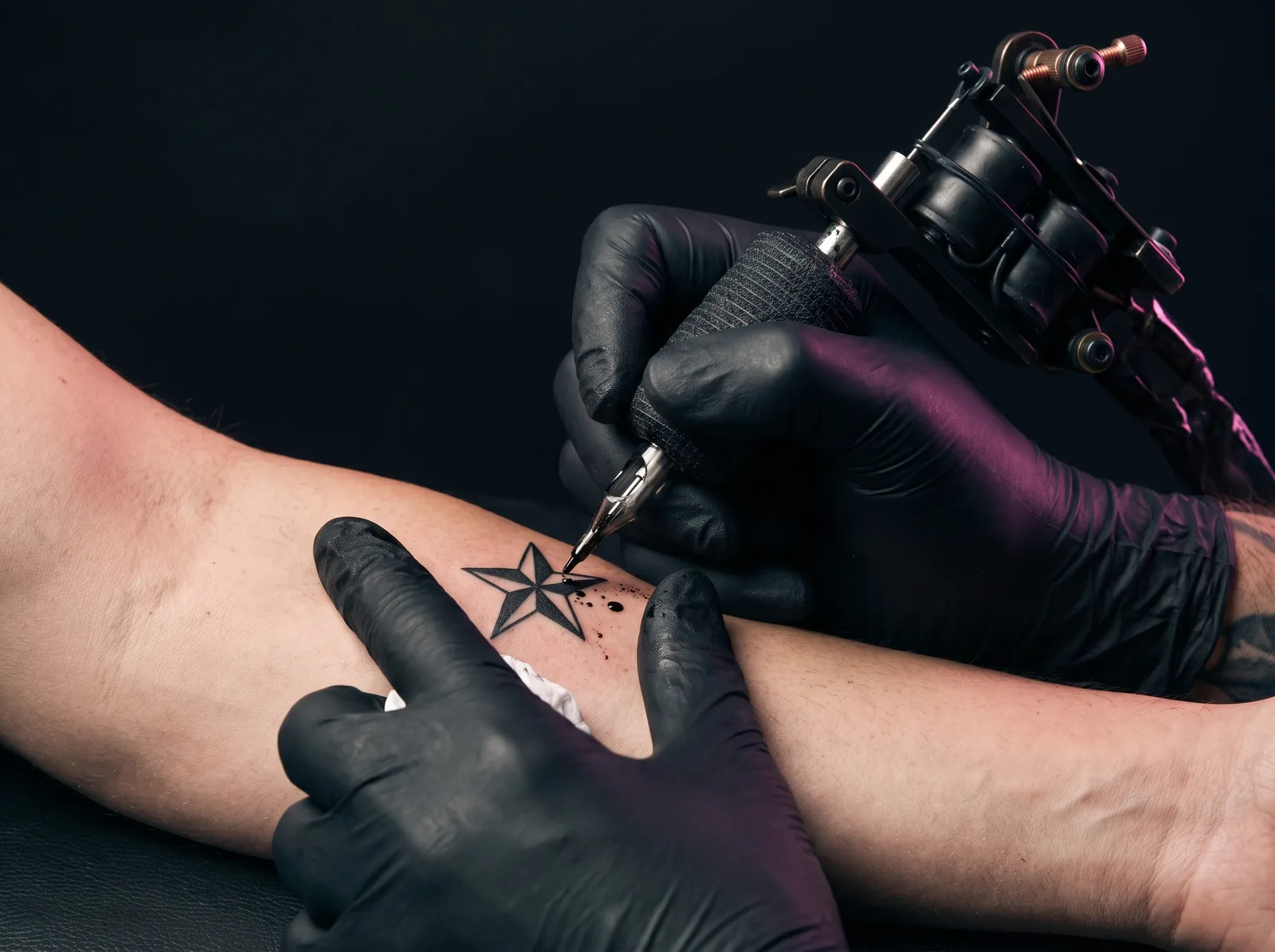 Tattoo artist tattooing a small bold flash star design on a client's forearm