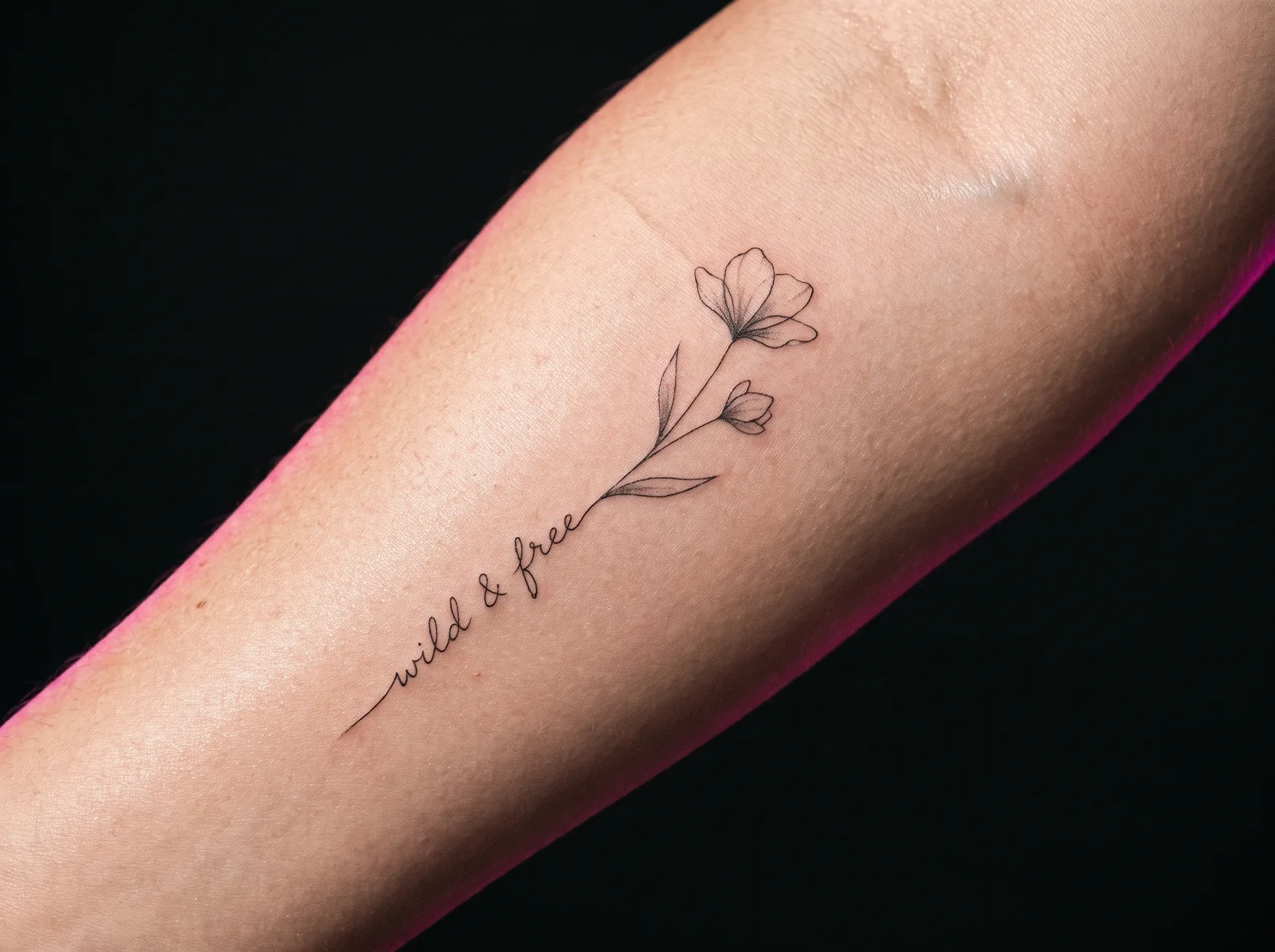 Healed fine-line minimalist tattoo of a wildflower and script on a forearm