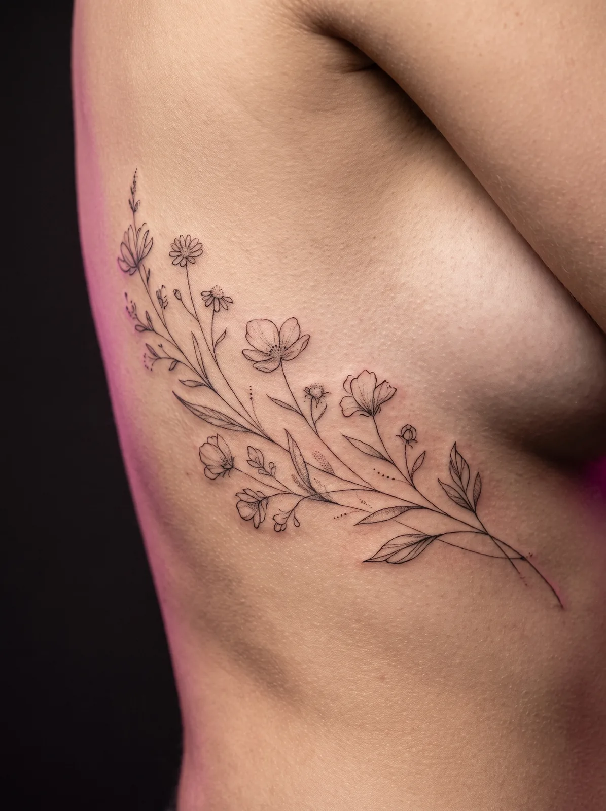 Healed fine-line botanical tattoo of trailing wildflowers along the ribs