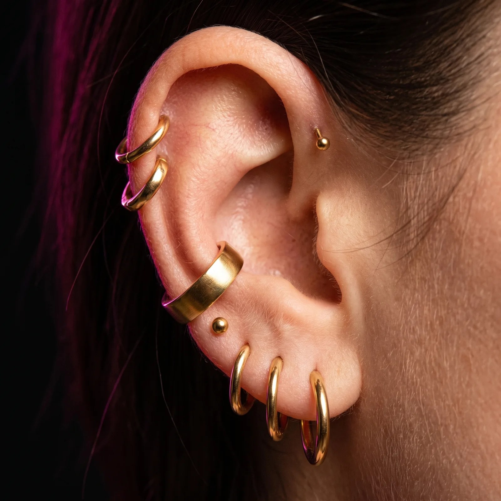 Close-up of layered gold hoops, an ear cuff, and studs on a healed ear stack