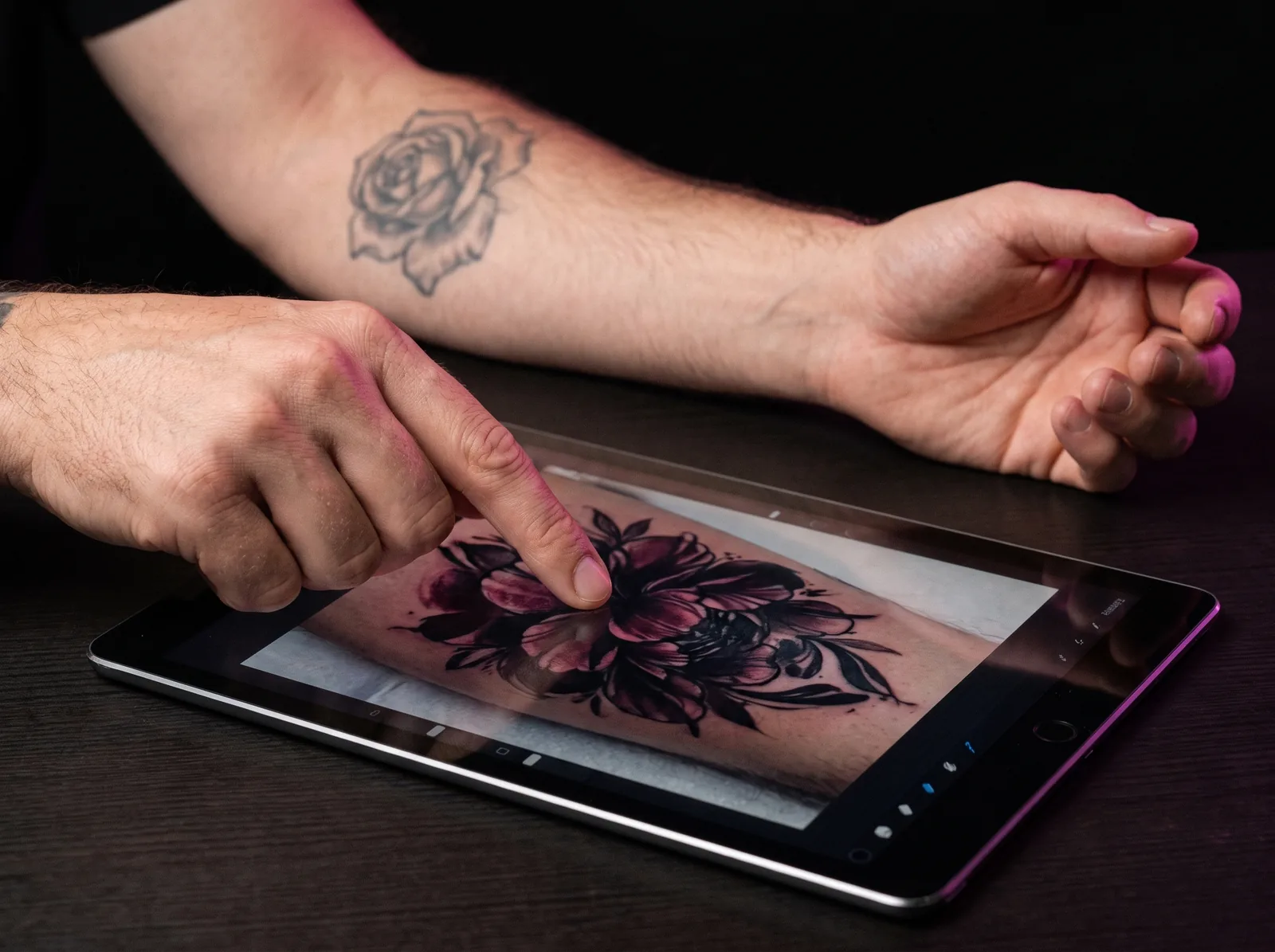 Hands reviewing a cover-up tattoo design mock-up on a tablet during a consultation