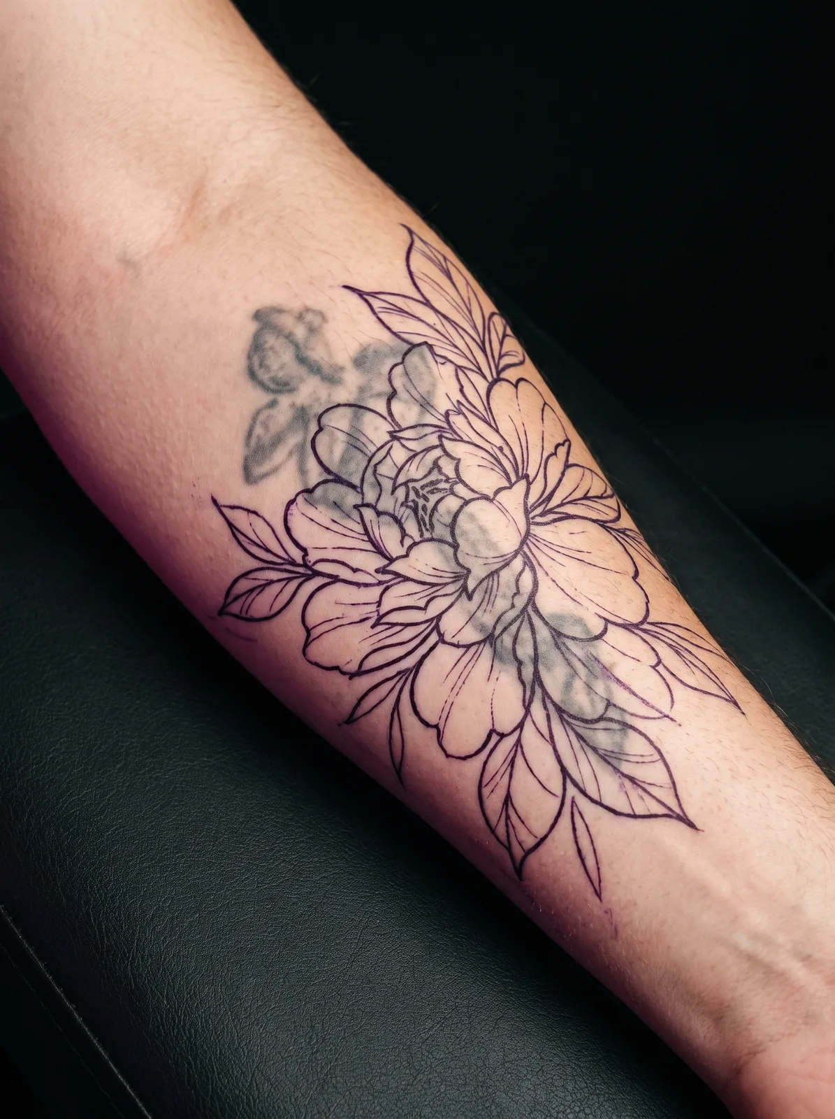 Fresh cover-up tattoo stencil outline drawn over a faded older tattoo on a forearm