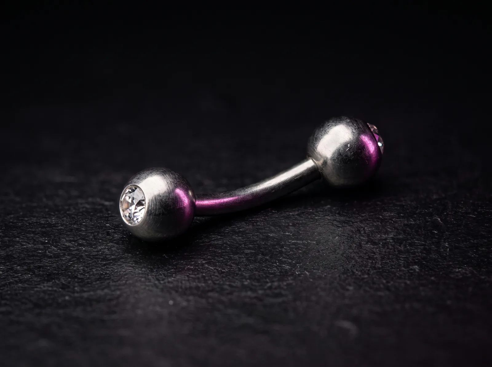 Implant-grade titanium curved barbell navel jewelry on a dark background