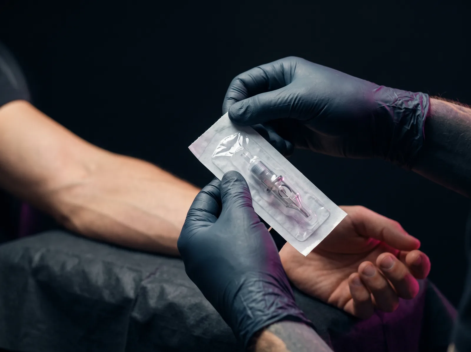 Gloved hands opening a sealed single-use sterile needle package in front of a client
